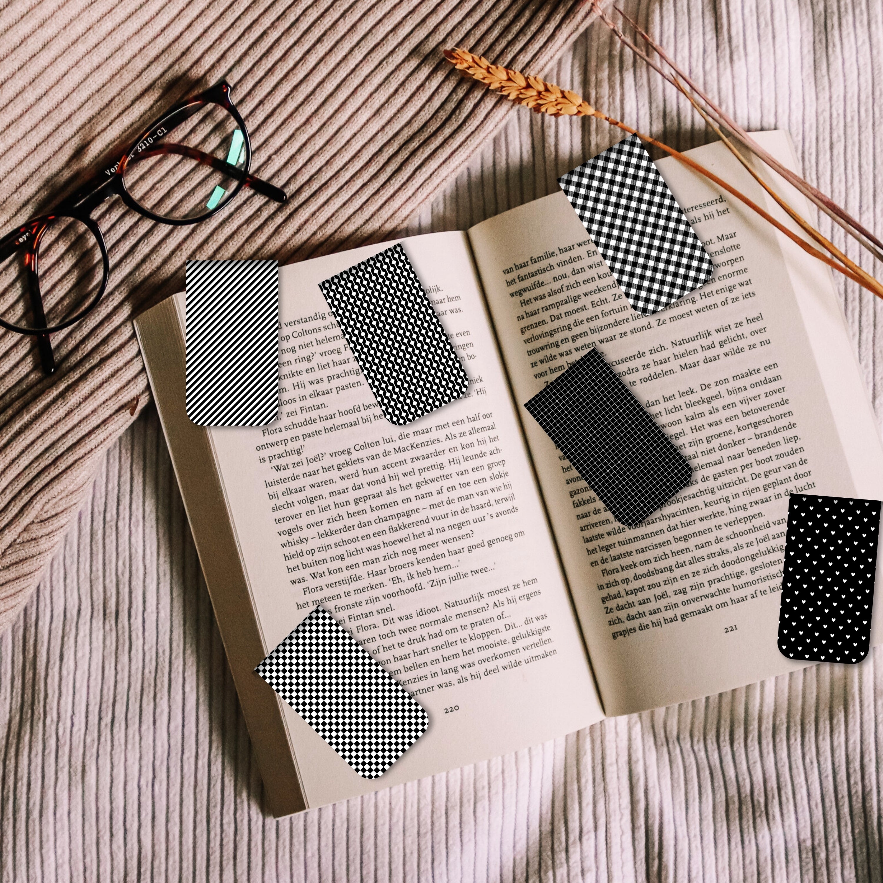 Black and white checkered bookmarks on an open book with glasses and dried plants.